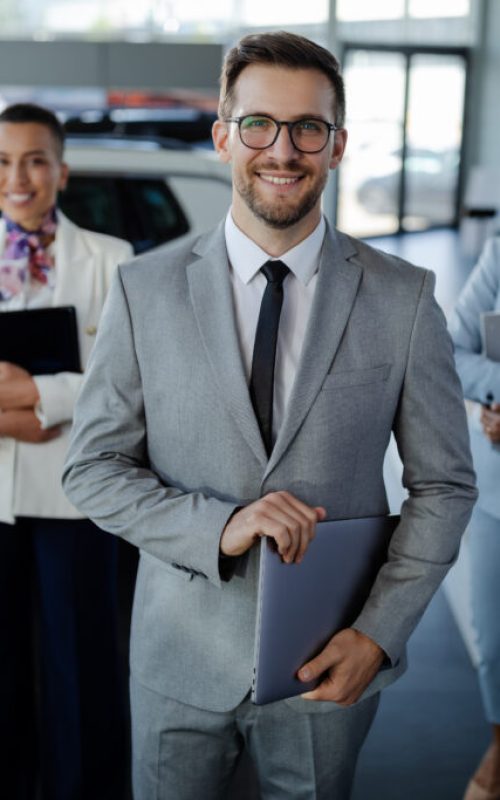 Confident salesteam in dealership, three beautiful consultants or managers in elegant suit looking on camera.