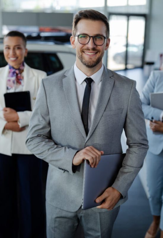 Confident salesteam in dealership, three beautiful consultants or managers in elegant suit looking on camera.
